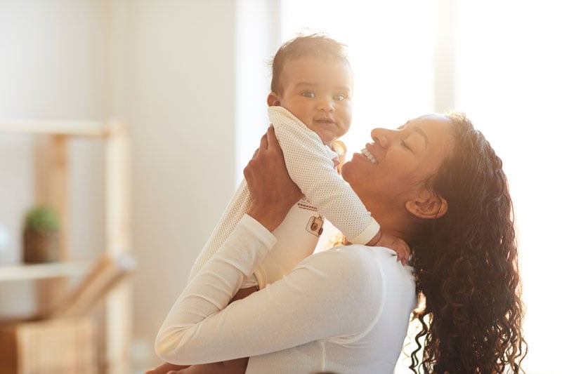 attractive-young-african-mother-standing-picking-bab-up-in-sunlight