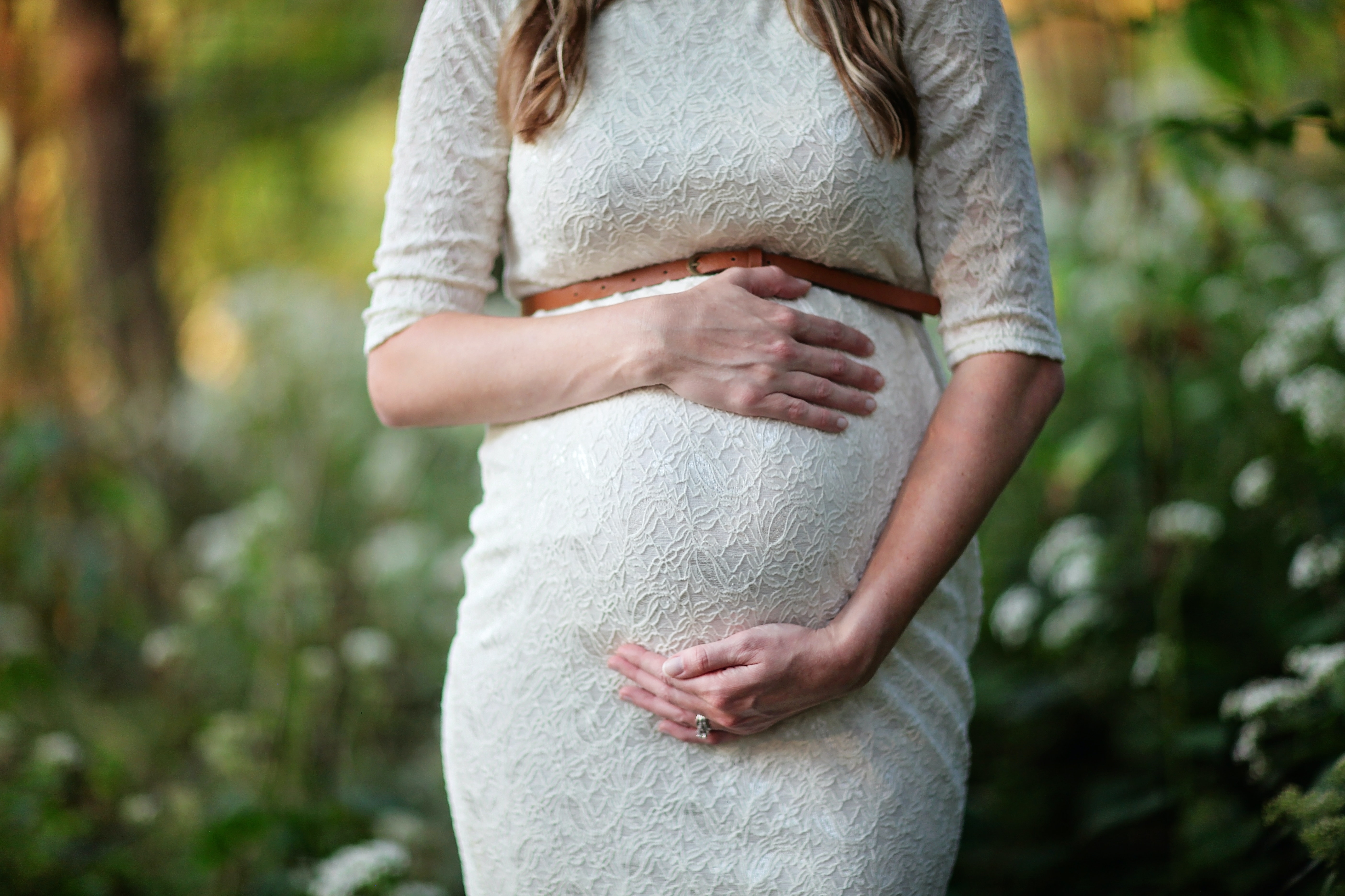 Pregnant woman in a white dress holding her belly.