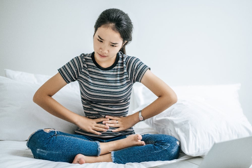 woman on bed with hands on stomach from fibroid pain